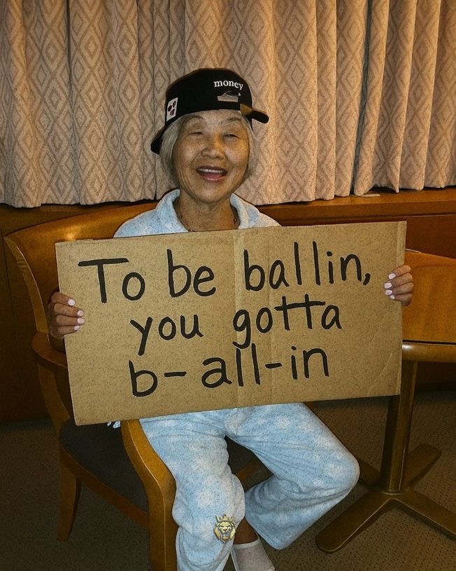 Grandma holding a sign that says 'To be ballin you gotta b-all-in'