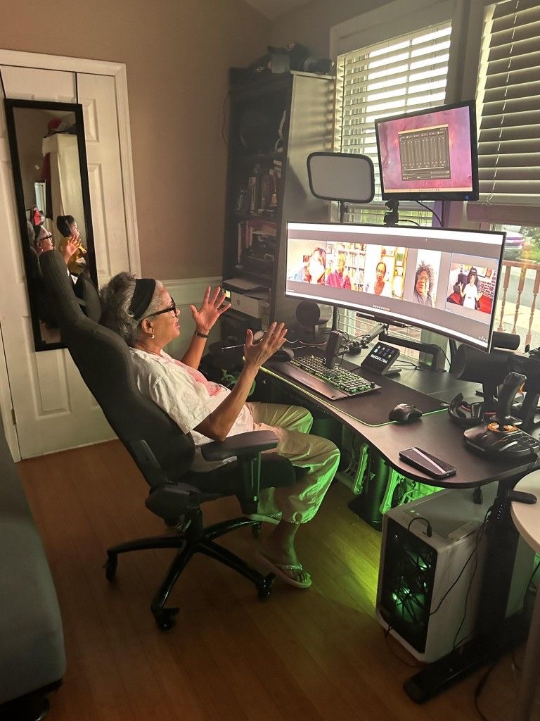 Grandmother in a home studio with monitors and audio gear, hands raised mid-session