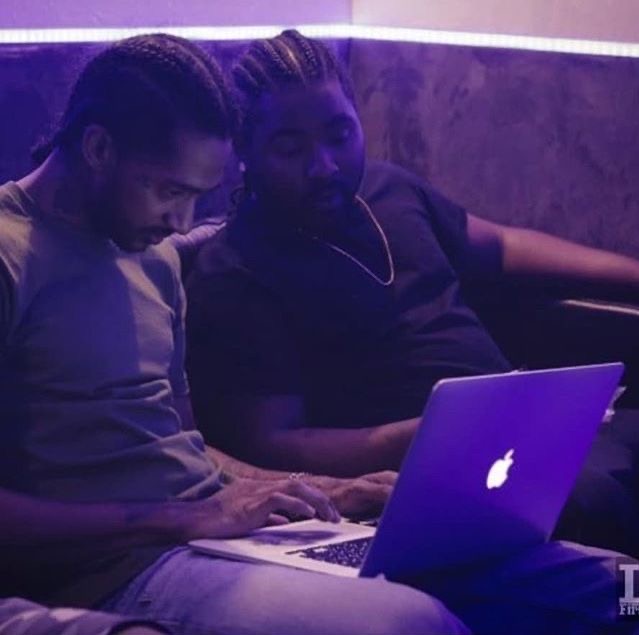 Two artists working on a laptop in a purple-lit studio